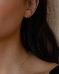 Close-up of a woman's ear adorned with a handmade Token Jewelry Loop Earring in 14K Gold Fill and a glimpse of a gold necklace.