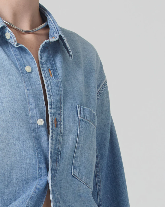 Close-up of a person wearing an oversized fit blue denim Kayla Shirt in Tide with a buttoned collar and chest pocket from Citizens of Humanity.