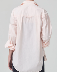 Rear view of a person wearing an Citizens of Humanity Kayla Shirt in Guava with a high-low hem, colored in light pink and white against a neutral background.