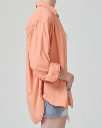 Side profile of a person wearing an oversized, peach-colored Kayla Shirt in Papaya with rolled-up sleeves and Citizens of Humanity denim shorts against a neutral background.