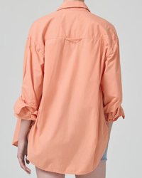 Woman wearing an oversized, coral-colored Citizens of Humanity Kayla Shirt in Papaya with a high-low hem, viewed from behind.