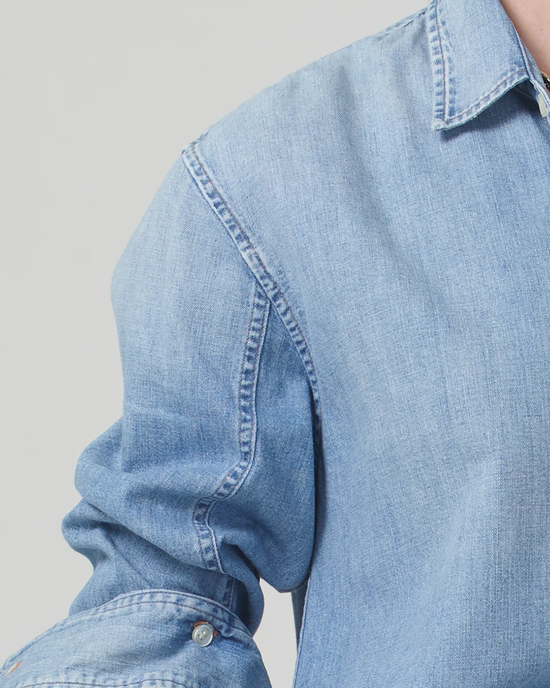 Close-up of a person wearing an oversized light blue denim "Shrunken Kayla Shirt in Tide" by Citizens of Humanity.