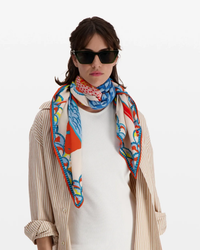 Woman posing in a striped shirt and white top with an oversized Inoui Editions bandana in Square 130 Tango Orange and sunglasses.