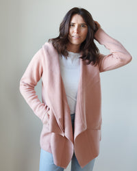 Woman in a casual pose wearing a pink Margaret O'Leary St Claire cashmere coat, white top, and light blue jeans.