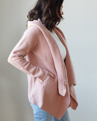 A woman in a Margaret O'Leary peach blazer and cashmere coat, facing to the side with an obscured face.