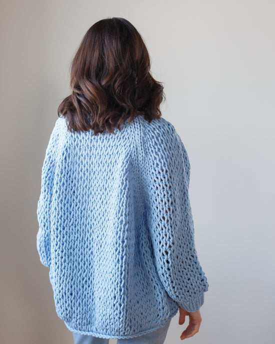 Woman wearing a Placid handknit cotton cardigan by Margaret O'Leary standing with her back to the camera.
