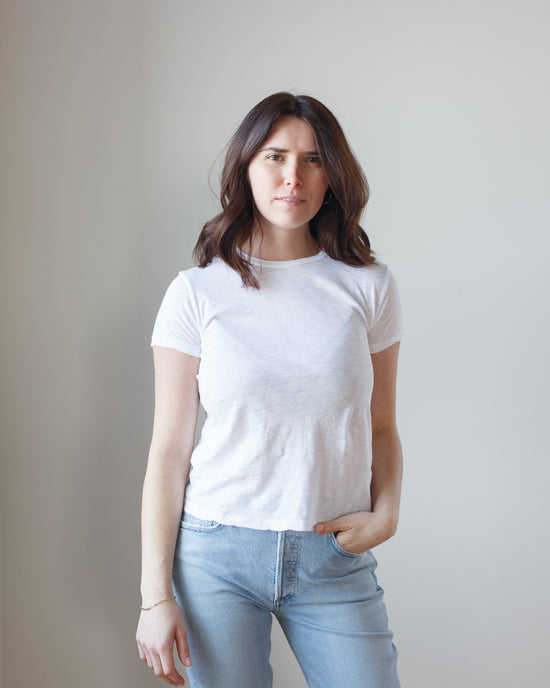 Woman standing against a plain background wearing a white Sierra S/S Crew Neck Top in White by Velvet by Graham & Spencer and blue jeans.
