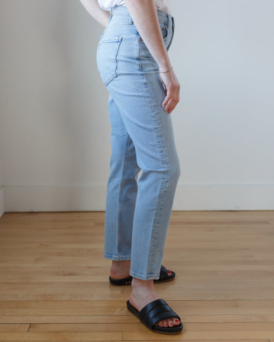 Person standing sideways wearing blue AGOLDE Riley Long in Issue high rise straight comfort stretch denim and black sandals.