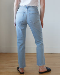 A person standing against a plain background, wearing blue comfort stretch denim AGOLDE Riley Long in Issue high rise straight jeans and black flats.
