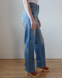Person standing in Tricia Wide Straight in Joyous blue jeans and wooden clogs against a plain background by AMO.