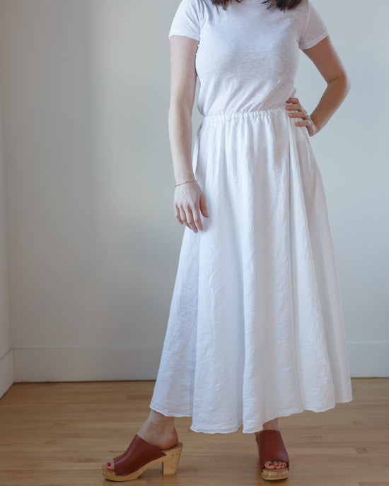 Woman standing in a CP Shades Deidra Skirt HW Linen Twill in White and brown sandals, with a hand on her hip.