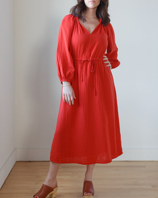 Woman in a red Audrey Dress in Cherry by Velvet by Graham & Spencer with long sleeves and a tie waist, crafted from cotton gauze, paired with brown open-toe heels.