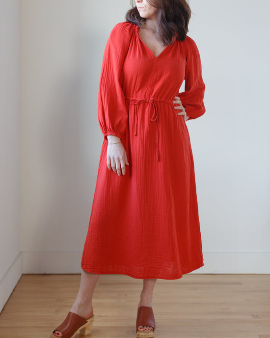 A person wearing a red Velvet by Graham & Spencer Audrey Dress in Cherry with long sleeves and brown heeled sandals.
