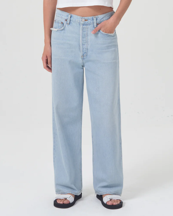Sentence with replaced product: Model showcasing a pair of light blue AGOLDE Low Slung Baggy in Shake jeans with sandals.