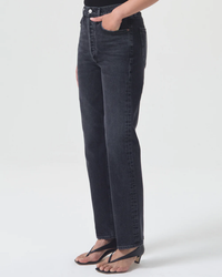 A person stands wearing dark blue AGOLDE High Rise Stovepipe jeans made of organic cotton denim and black sandals.