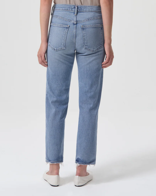 Woman standing, featuring the back view of a pair of light-wash AGOLDE Kye in Foreseen jeans with frayed hems.
