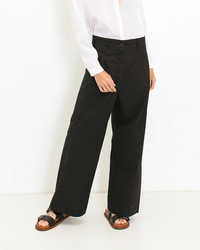 Person wearing a white 100% cotton shirt from A Shirt Thing, black wide-leg pants, and brown sandals against a plain background.