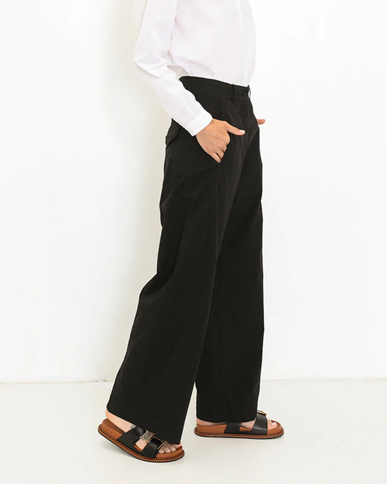A person standing side profile wearing Marnie high waist black straight leg trousers, a white shirt from A Shirt Thing, and brown sandals.