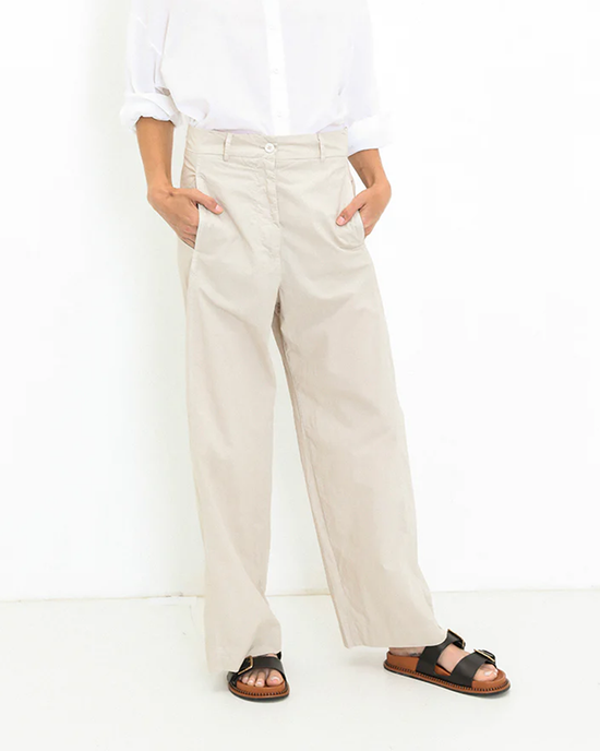 Person standing in a Marnie - Parachute in Sand shirt by A Shirt Thing and beige high waist, straight leg trousers with one hand in pocket, paired with black and brown sandals.