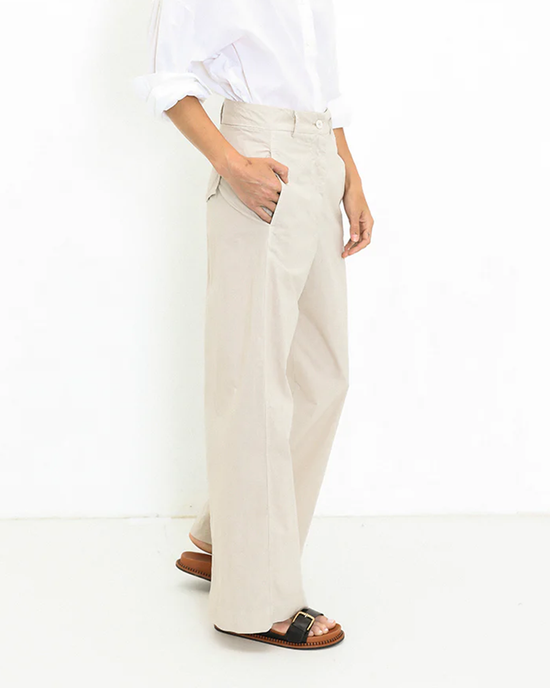 Person standing in a white A Shirt Thing shirt and beige high-waist, straight-leg trousers with one hand in pocket wearing the Marnie - Parachute in Sand pants.