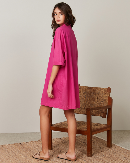 A woman in a magenta Hartford Rimo dress with oversized short sleeves standing beside a wooden chair.