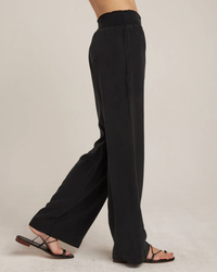 A person standing side-on wearing black TENCEL™ Lyocell, Bella Dahl Smocked Waist Wide Leg in Vintage Black pants, and strappy sandals.