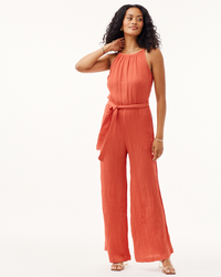 Woman posing in a Bella Dahl Smocked Back Cami Jumpsuit Crinkle in Papaya Red with her hand on her neck.