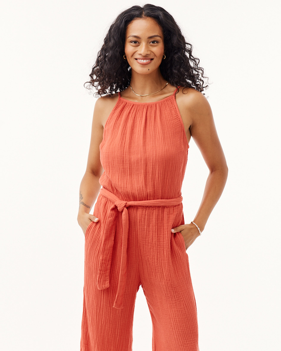 A smiling woman standing with hands on hips, wearing a Bella Dahl Smocked Back Cami Jumpsuit Crinkle in Papaya Red color, featuring a wide leg and a tie waist.