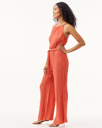 Woman wearing a Bella Dahl Smocked Back Cami Jumpsuit Crinkle in Papaya Red standing in a poised posture.