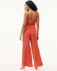Woman posing in a Bella Dahl Smocked Back Cami Jumpsuit Crinkle in Papaya Red with wide-leg pants.