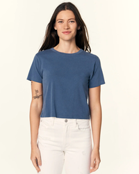 A woman in an AMO Babe Tee in Deep Indigo and Amo Denim standing against a neutral background.