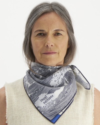 A woman with gray hair wearing a beige top and an Inoui Editions Square 65 Oceanique in Navy bandana.
