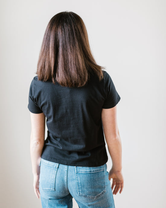 A person seen from behind wearing a Velvet by Graham & Spencer Frankie Tee in Black and blue high rise straight leg jeans against a white background.