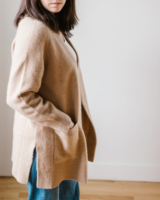 Woman in a beige Margaret O'Leary Luxe Sweater Coat in Camel and jeans standing against a neutral background.