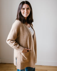 Woman smiling at the camera while wearing a Margaret O'Leary Luxe Sweater Coat in Camel and white top.