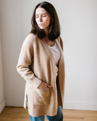Woman in a Margaret O'Leary Luxe Sweater Coat in Camel and jeans standing against a plain background.