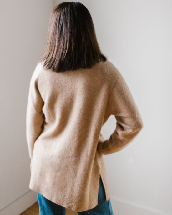 A person wearing a Margaret O'Leary Luxe Sweater Coat in Camel and blue jeans standing with their back to the camera.