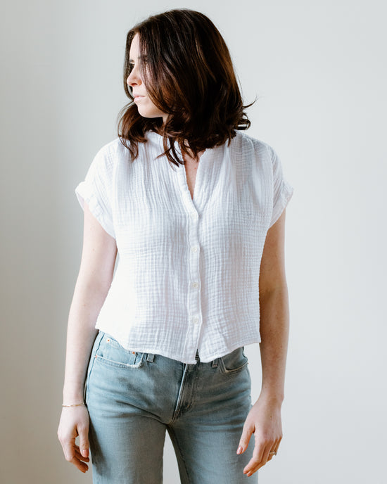 A woman in a Felicite Apparel white Short Sleeve Top and blue jeans standing against a plain background.