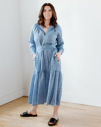 Woman standing in a room wearing a Puff Sleeve Maxi Dress in Sky by Felicite Apparel and black slides.