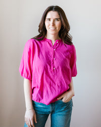 A woman in a Hartford Hibiscus Turette Shirt with a mandarin collar and jeans standing against a neutral background, smiling at the camera.