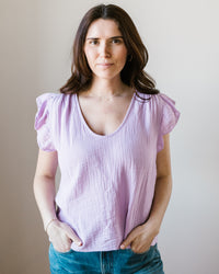 A woman in a Remi Flutter Slv Top in Thistle from Velvet by Graham & Spencer and jeans standing against a neutral background.