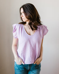 Woman in a Velvet by Graham & Spencer Remi Flutter Slv Top in Thistle and blue jeans standing against a neutral background.