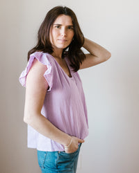 A woman in a Remi Flutter Slv Top in Thistle by Velvet by Graham & Spencer and blue jeans posing with one hand on her hip against a neutral background.