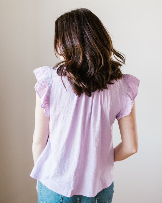 A woman standing with her back to the camera wearing a pink Remi Flutter Slv Top in Thistle by Velvet by Graham & Spencer and blue jeans.