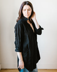A woman in a CP Shades Teton in Black Heavy Weight Linen Twill blouse touching her hair with a contemplative expression.