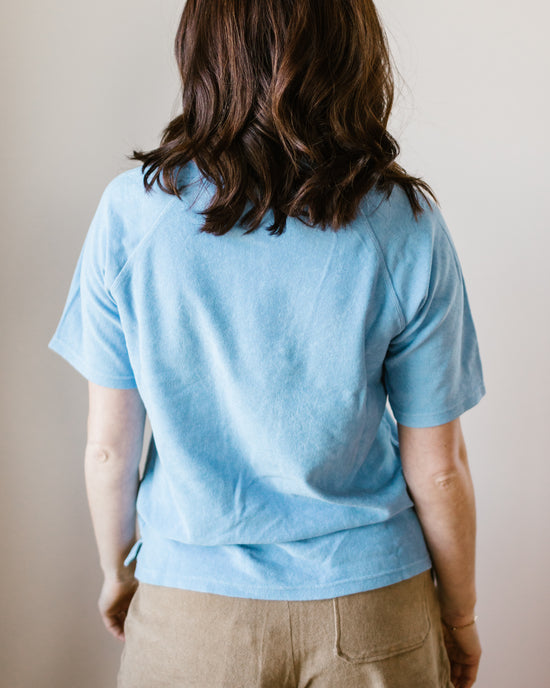 Woman standing with her back to the camera wearing a Hartford Temery Shirt in Wave and beige pants.