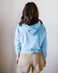 A person viewed from behind wearing a Hartford Tarol Hoody in Wave and beige shorts against a neutral background.