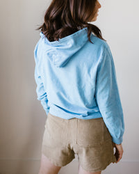 A person wearing a Hartford Tarol Hoody in Wave and beige shorts standing with their back to the camera.