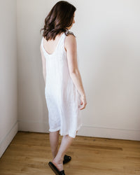 Woman in a CP Shades Dayna Dress in White HW Linen Twill standing with her back turned to the camera.