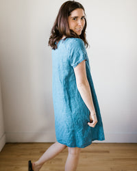 Woman in blue CP Shades Esme Dress w/o Pockets in Bleach Indigo Twill walking and looking back over her shoulder.